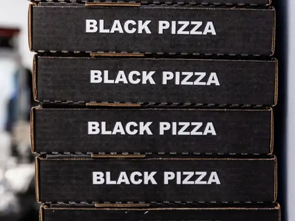 A stack of pizza boxes with the Black Pizza branding on the side. 