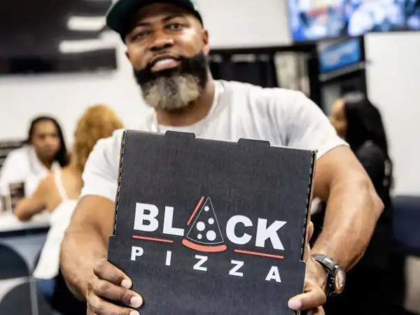 Business owner displaying a pizza box with Black Pizza logo. 