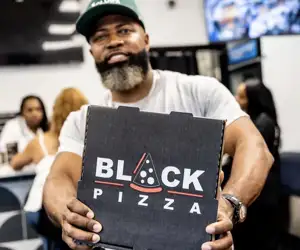 Business owner displaying a pizza box with Black Pizza logo. 