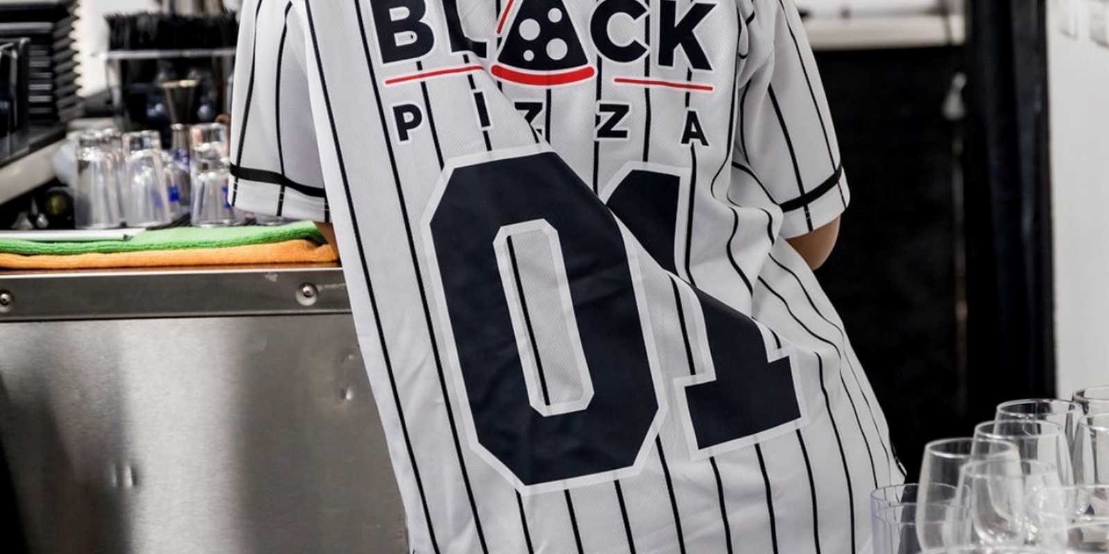 Guest wearing a baseball uniform with sponsorship from Black Pizza on the back.