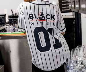 Guest wearing a baseball uniform with sponsorship from Black Pizza on the back. 