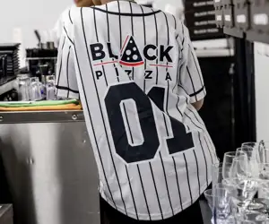 Guest wearing a baseball uniform with sponsorship from Black Pizza on the back. 